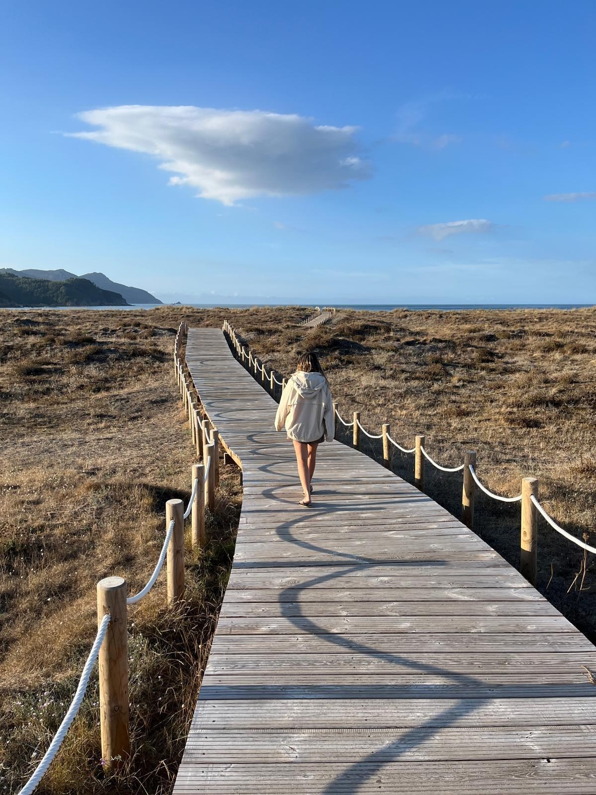 Alicia caminando por una pasarela entre dunas junto al mar
