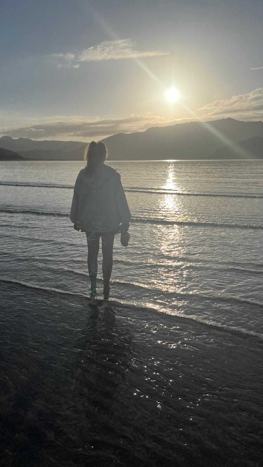 Alicia de espaldas frente al mar, mirando la luz del sol en una playa de Galicia